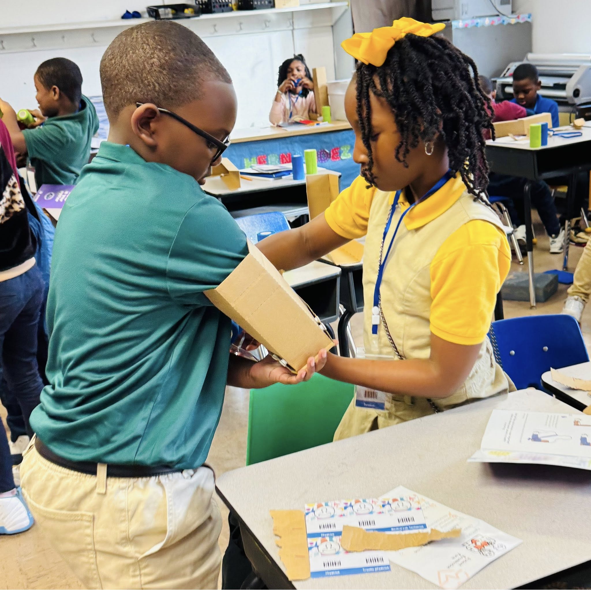 A girl putting a cardboard splint on a boy's arm.